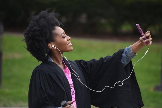 Photo of a female 波胆网站 student in graduation robes, taking a selfie and smiling